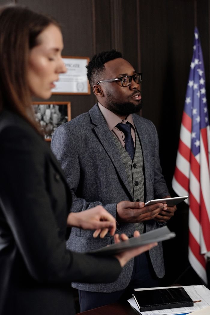 Business professionals discussing in an office with American flag backdrop, conveying a diplomatic setting.
