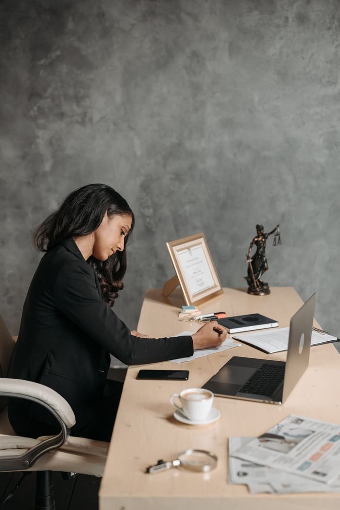 Businesswoman writing at desk with laptop and coffee in a modern office setting.